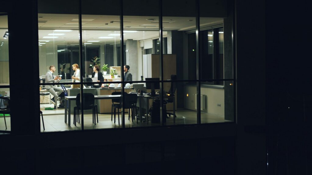 A nighttime office meeting with professionals working in a modern glass-walled office.