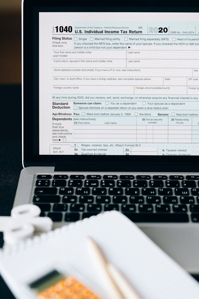 Close-up of a tax form on a laptop screen with a calculator and notebook in the foreground.