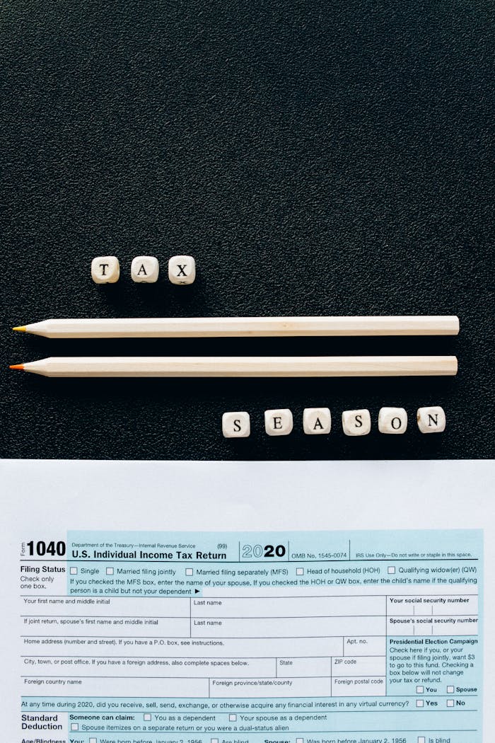 Creative composition featuring 1040 tax form, pencils, and letters spelling 'Tax Season' on black background.